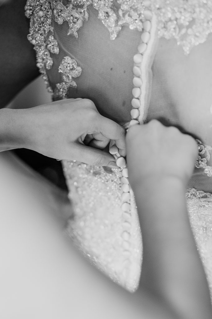 Trauzeugin hilft der Braut beim Schließen des Hochzeitskleides