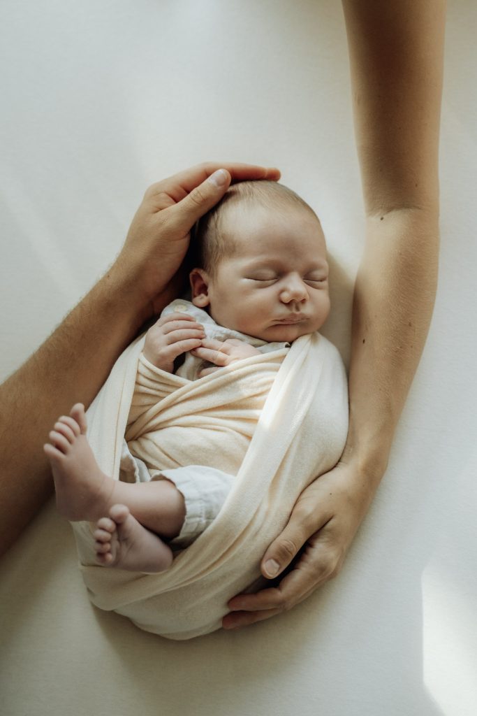 Erwachsene Hand sichert den Kopf eines Babys beim Fotoshooting