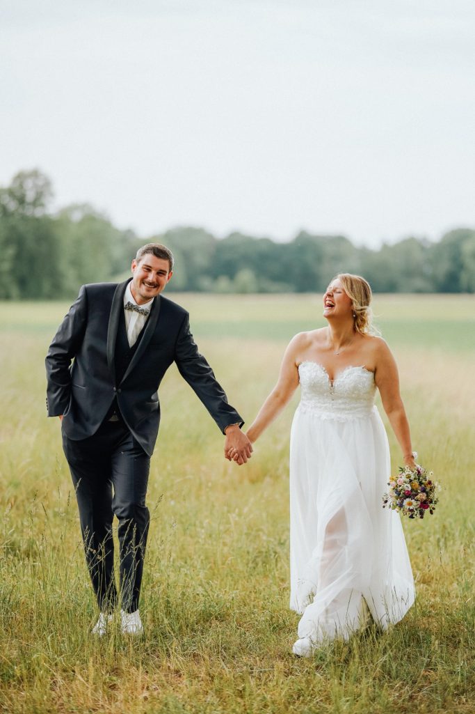 Hochzeitsfotograf Bielefeld Brautpaar läuft Hand in Hand Feld