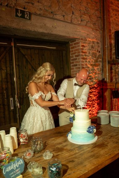Brautpaar schneidet gemeinsam die Hochzeitstorte im Hof Steffen an
