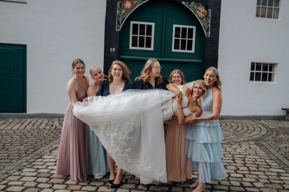 Braut zeigt gemeinsam mit ihren Begleiterinnen das Hochzeitskleid