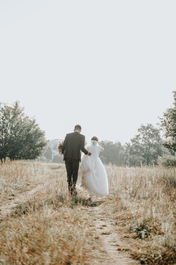 Hochzeitsfotograf Gütersloh Brautpaar läuft durch Feld Sonnenlicht